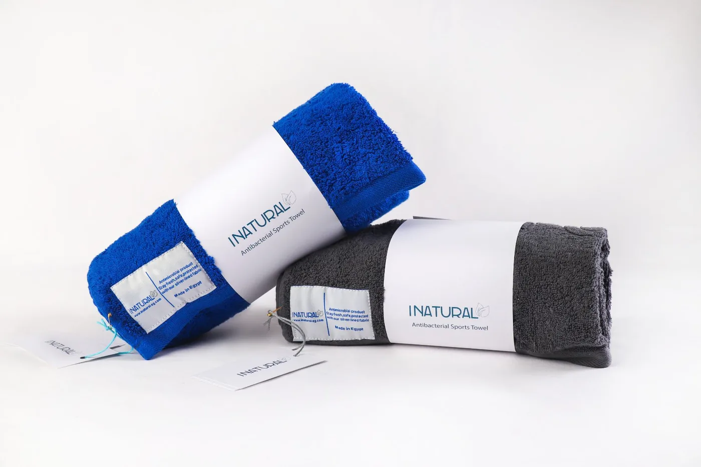 Two rolled INATURAL sports towels, one blue and one charcoal, in their printed INATURAL bands